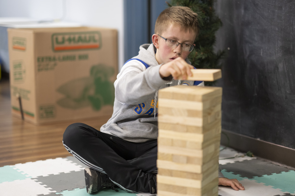 Young boy wearing glasses stacking Jenga blocks.