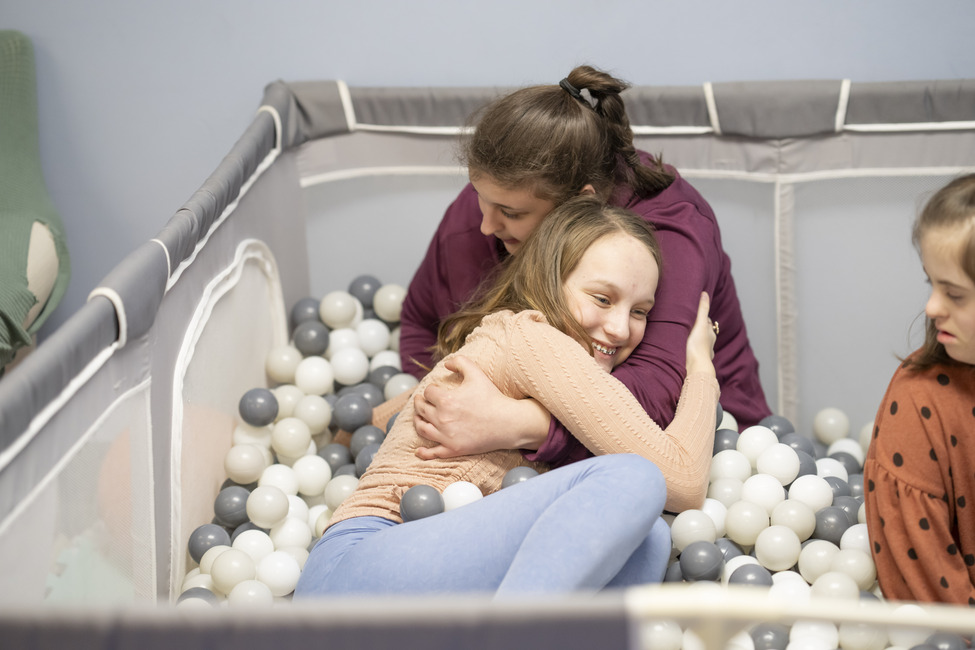 Young girl and staff person embracing in a ball pit.