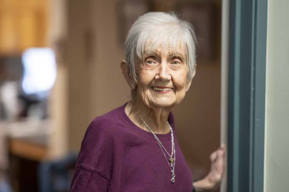 Senior woman smiling standing in an apartment doorframe.